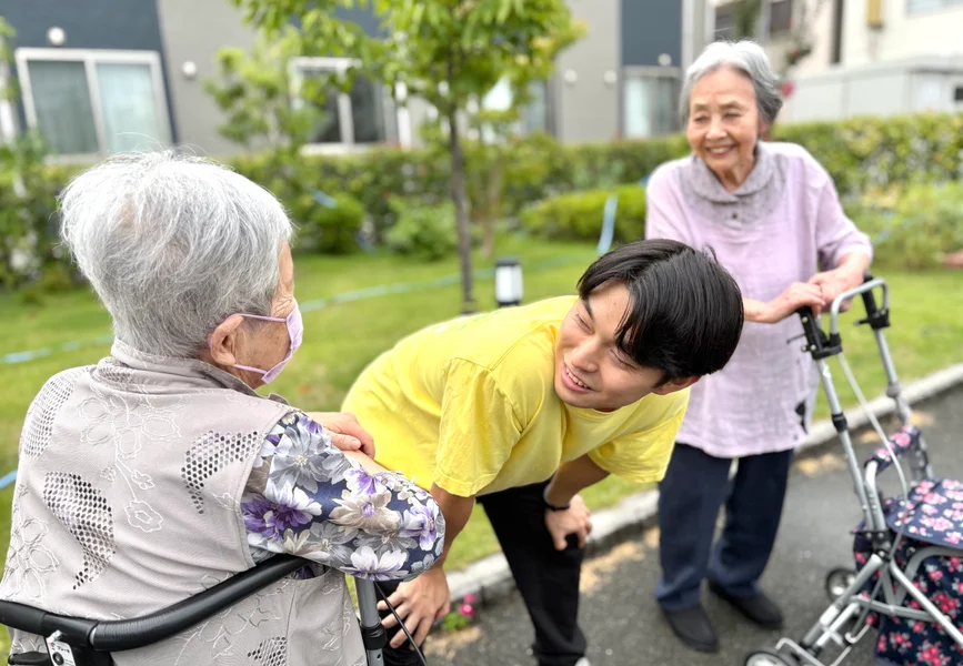 スタッフが入居者と花の世話をしている様子。屋外の庭園活動。